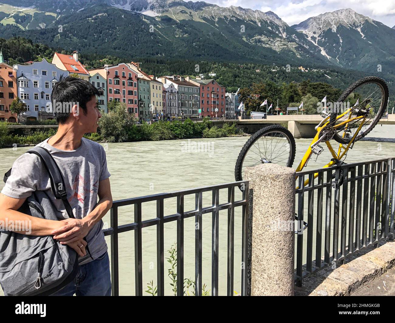 An Asian tourist stands by the river Inn in Innsbruck. He is looking at a railing on which an upside down bicycle is parked. Stock Photo