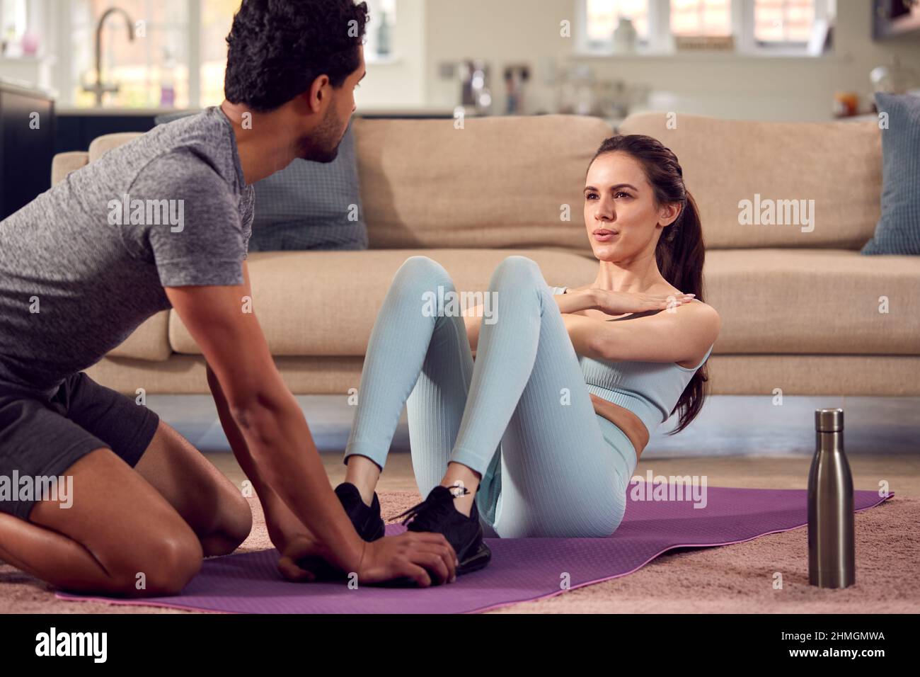 Woman With Male Personal Trainer Doing Sit Ups As Part Of Exercising At Home Stock Photo