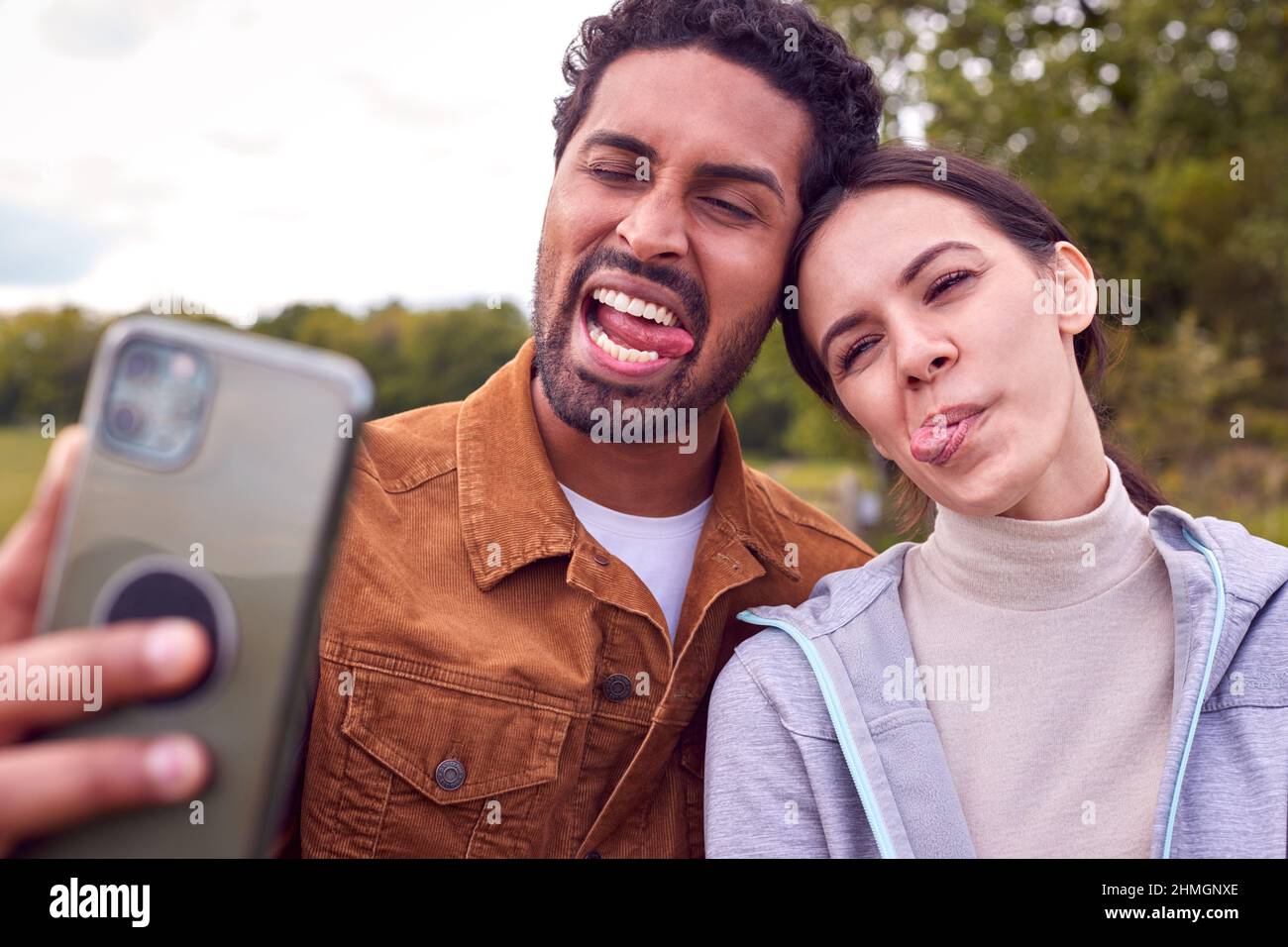 Couple On Walk In Countryside Pulling Funny Faces As They Take Selfie On Mobile Phone Stock Photo