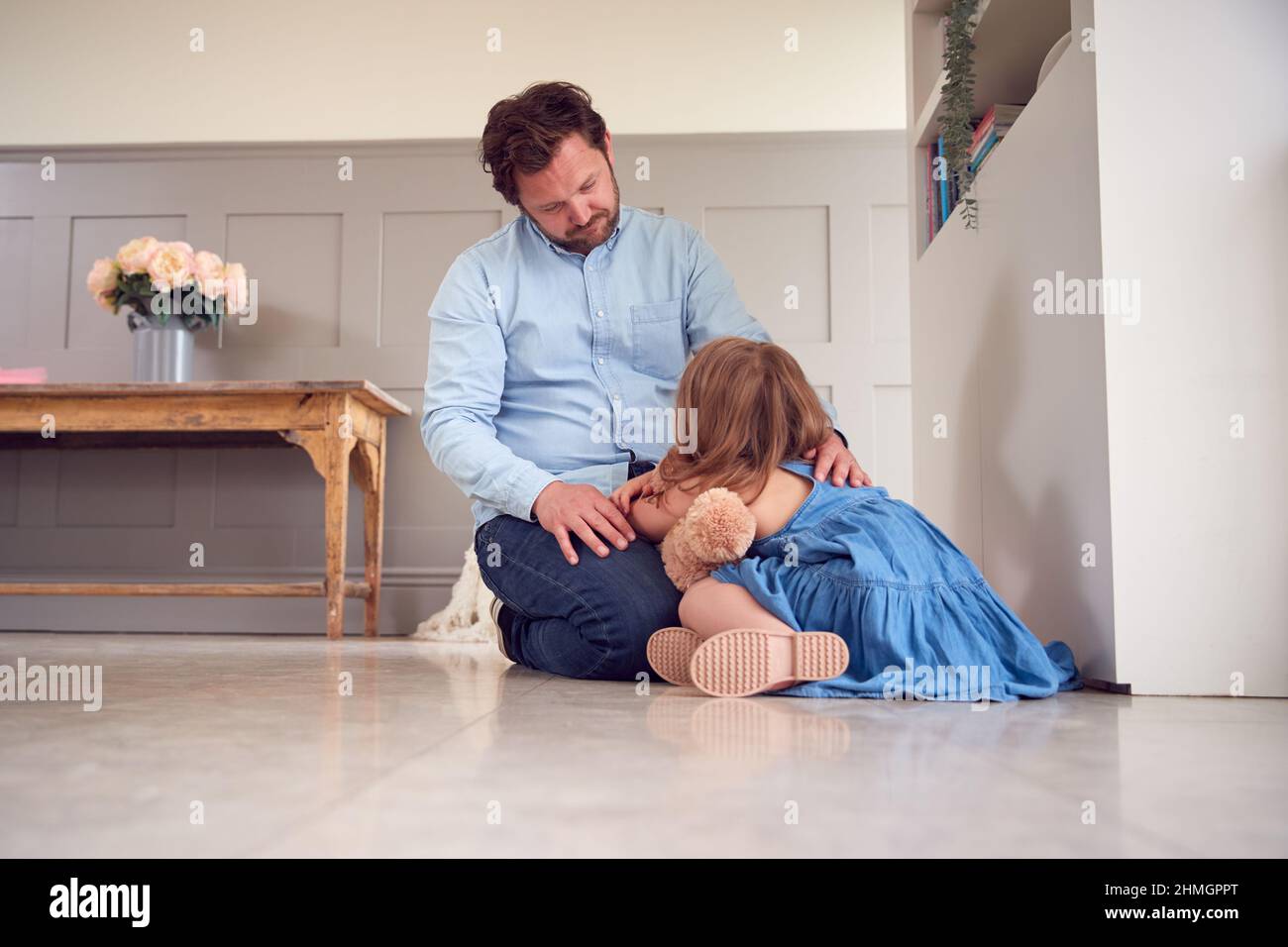 Father Comforting Unhappy Daughter Sitting On Floor Holding Teddy Bear