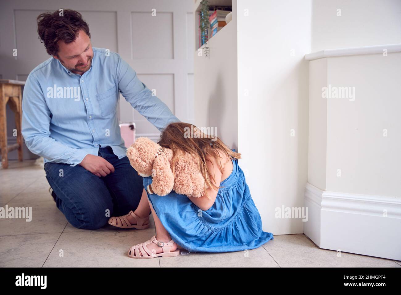 Father Comforting Unhappy Daughter Sitting On Floor Holding Teddy Bear