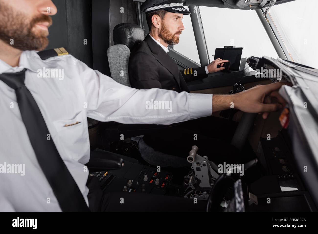 captain in cap and uniform using device with blank screen near co-pilot ...