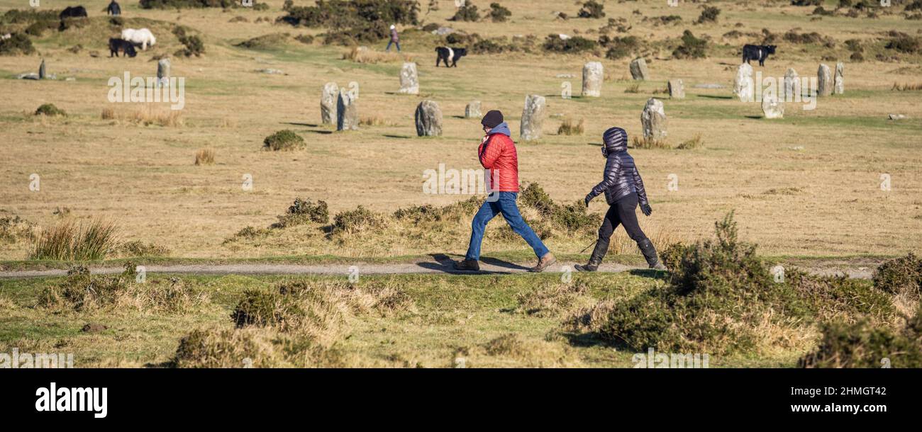 A panoramic image of people walking past the Standing stones known as the Hurlers Neolithic Bronze Age stone circles on Minion Downs on Bodmin Moor in Stock Photo