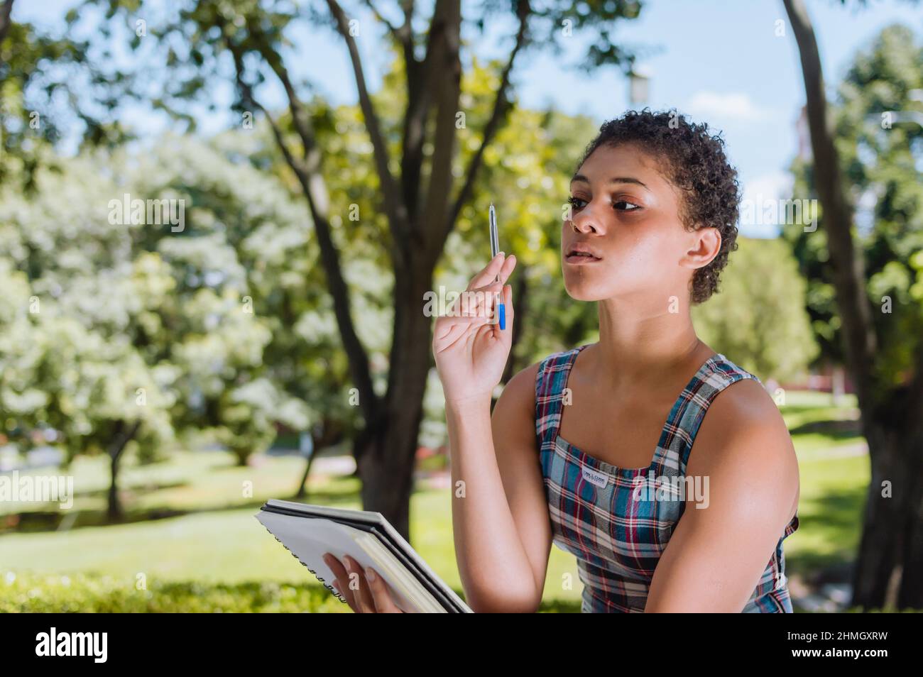 young brunette argentinian girl is sitting in a square concentrated, paying attention, thinking and studying taking note in a notebook with a pen, wit Stock Photo