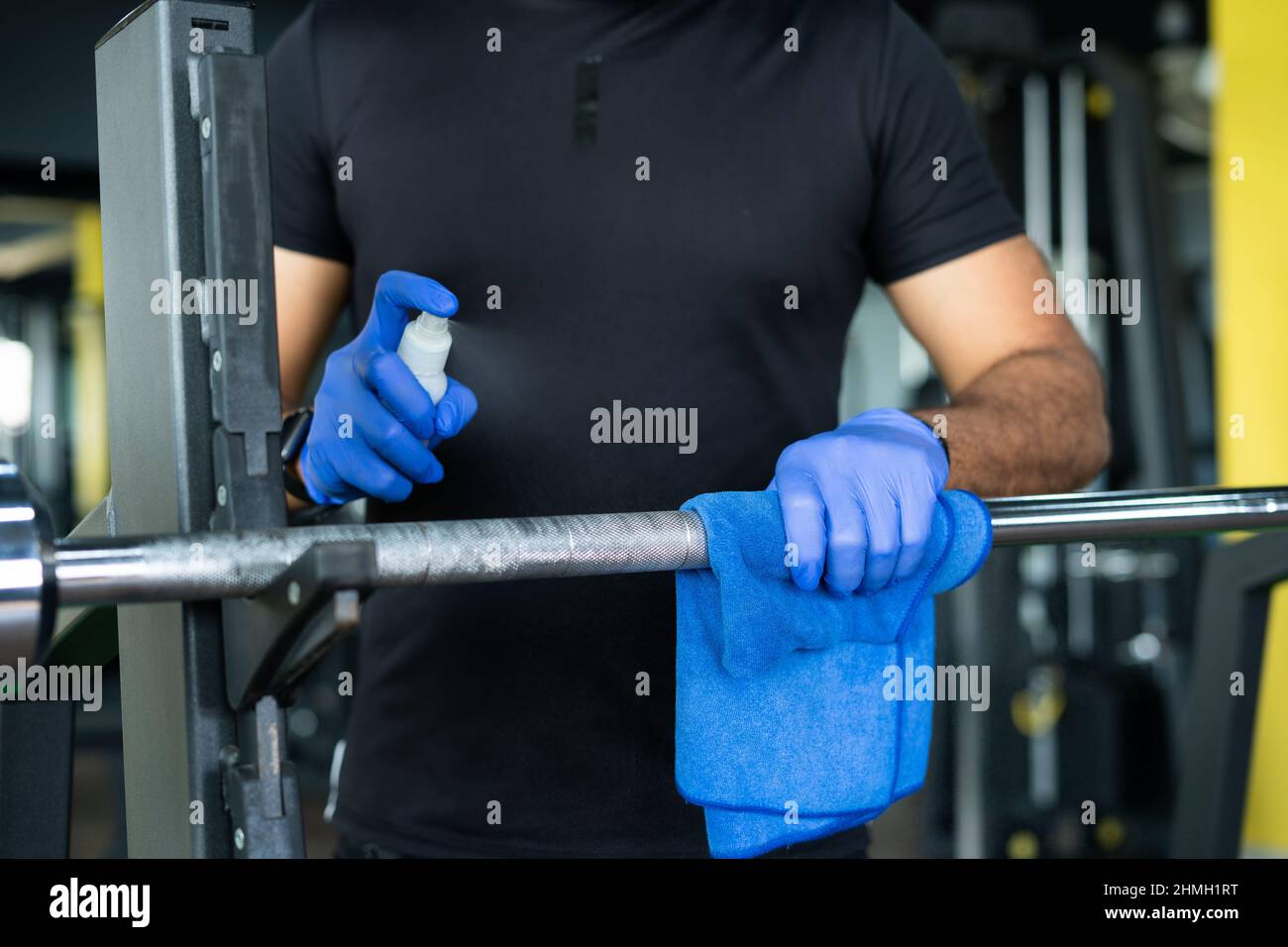 close up shot of hands with gloves sanitizing or wiping sweat of weight ligting rod or gym equipment due to coronavirus - concept of covid-19 Stock Photo
