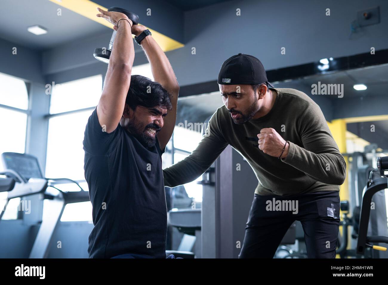 focus on client, Trainer motivating athlete to push his limits during workout at gym - concept of intense exercise, bodybuilding, determination and Stock Photo