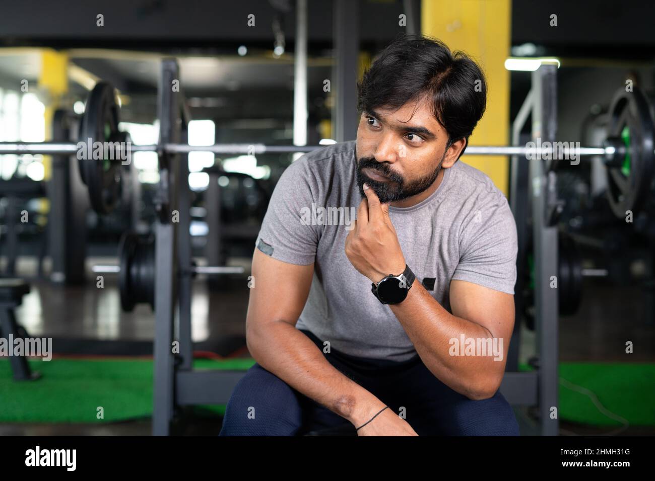 Young Indian athlete thinking or resting at gym after wrokout - Concept of thoughtful, relaxation and fitness center. Stock Photo