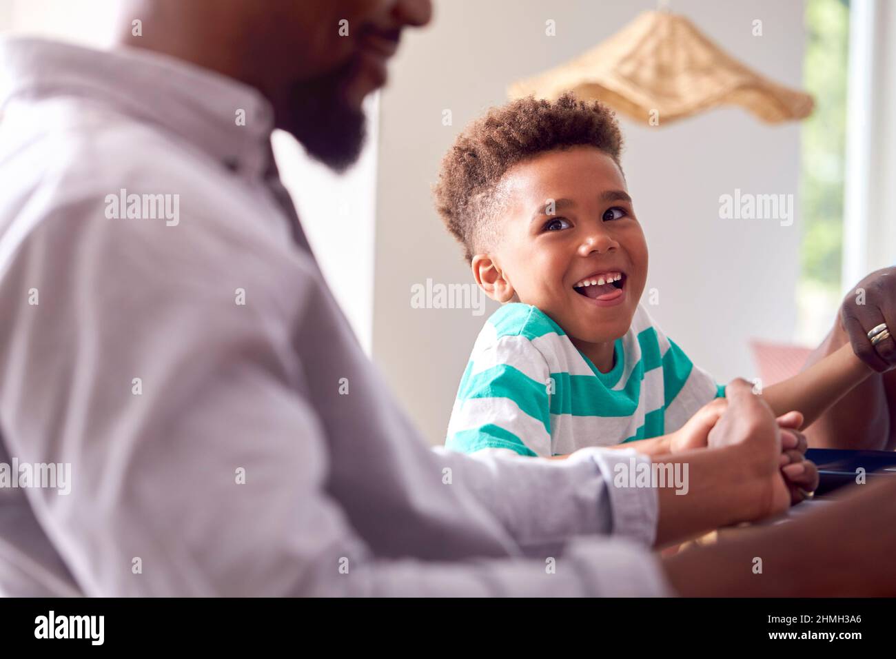 Son With Father And Grandfather Joining Hands To Say Grace Before Multi-Generation Family Meal Stock Photo