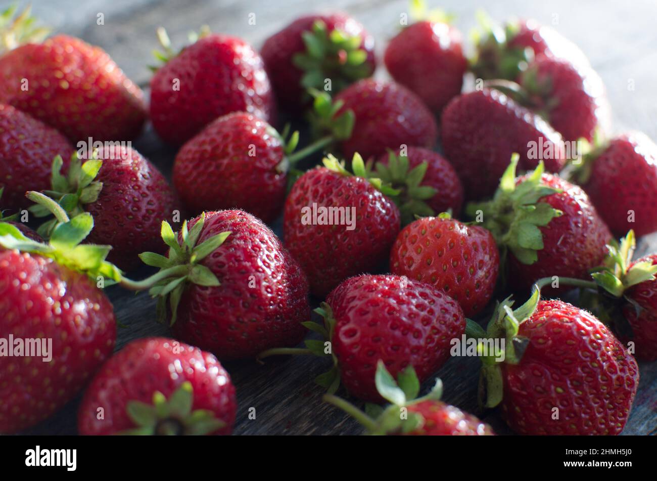 Ripe red strawberries controlam bright light on the old wooden table ...