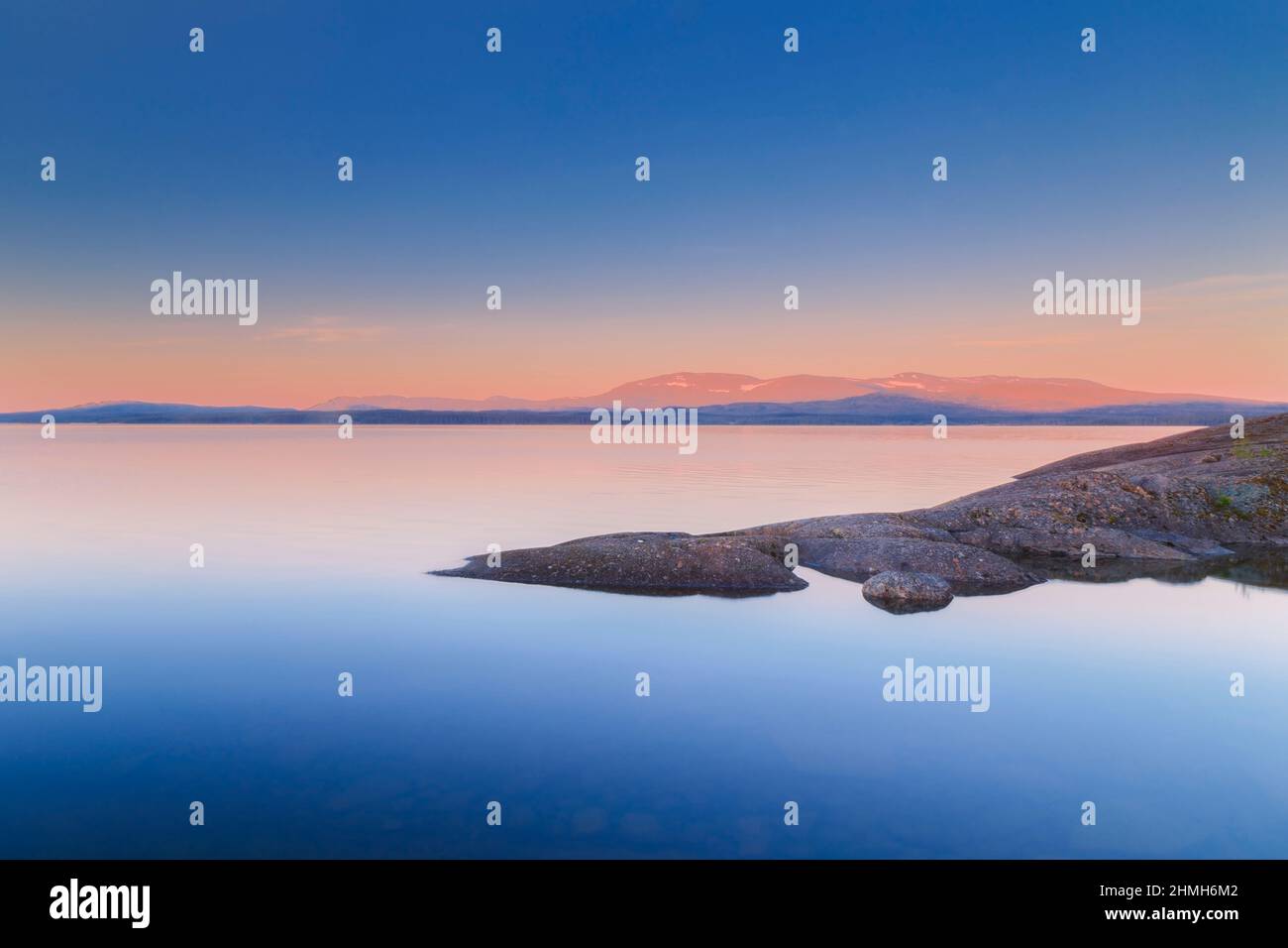 rocks in water with little snow left on mountains during sunset Stock Photo