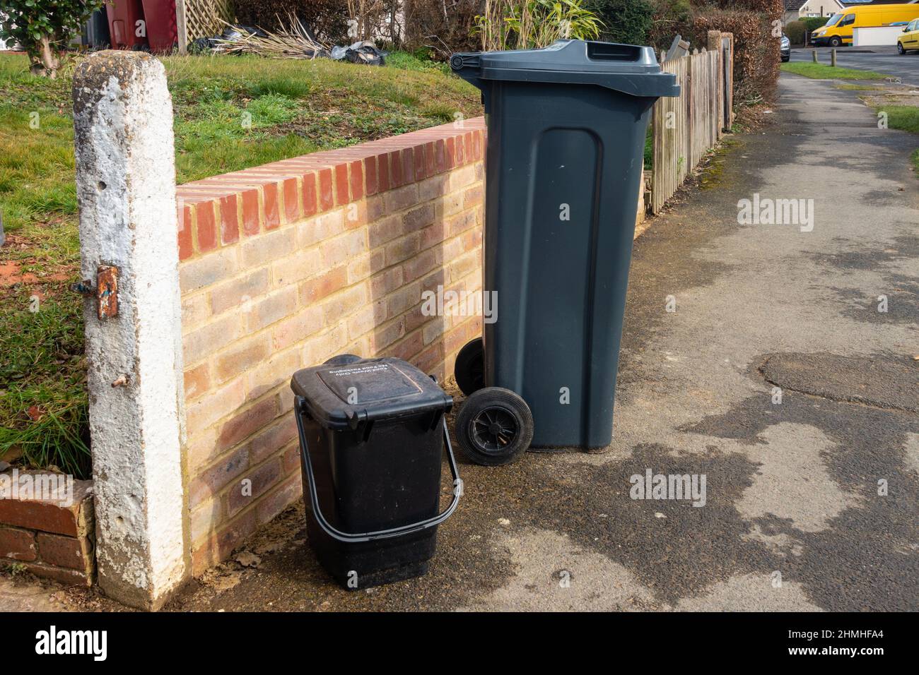 A black wheelie bin and waste food caddy on a pavement outside the