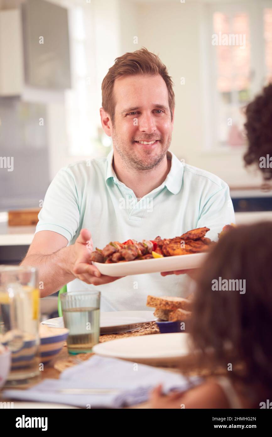 Father Serving Food Sitting Around Table For Family Meal At Home Stock