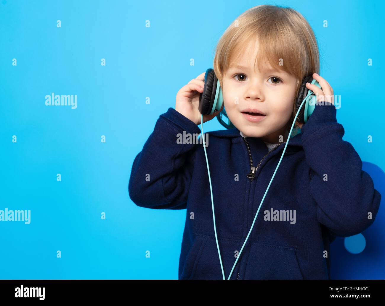adorable small three years old boy wearing headphones on blue