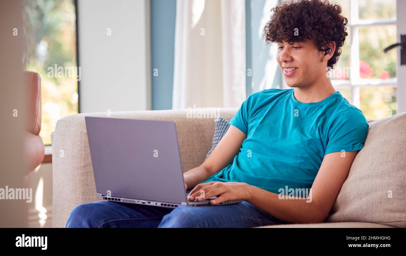Teenage Boy Sitting On Sofa At Home Using Laptop Computer Stock Photo ...