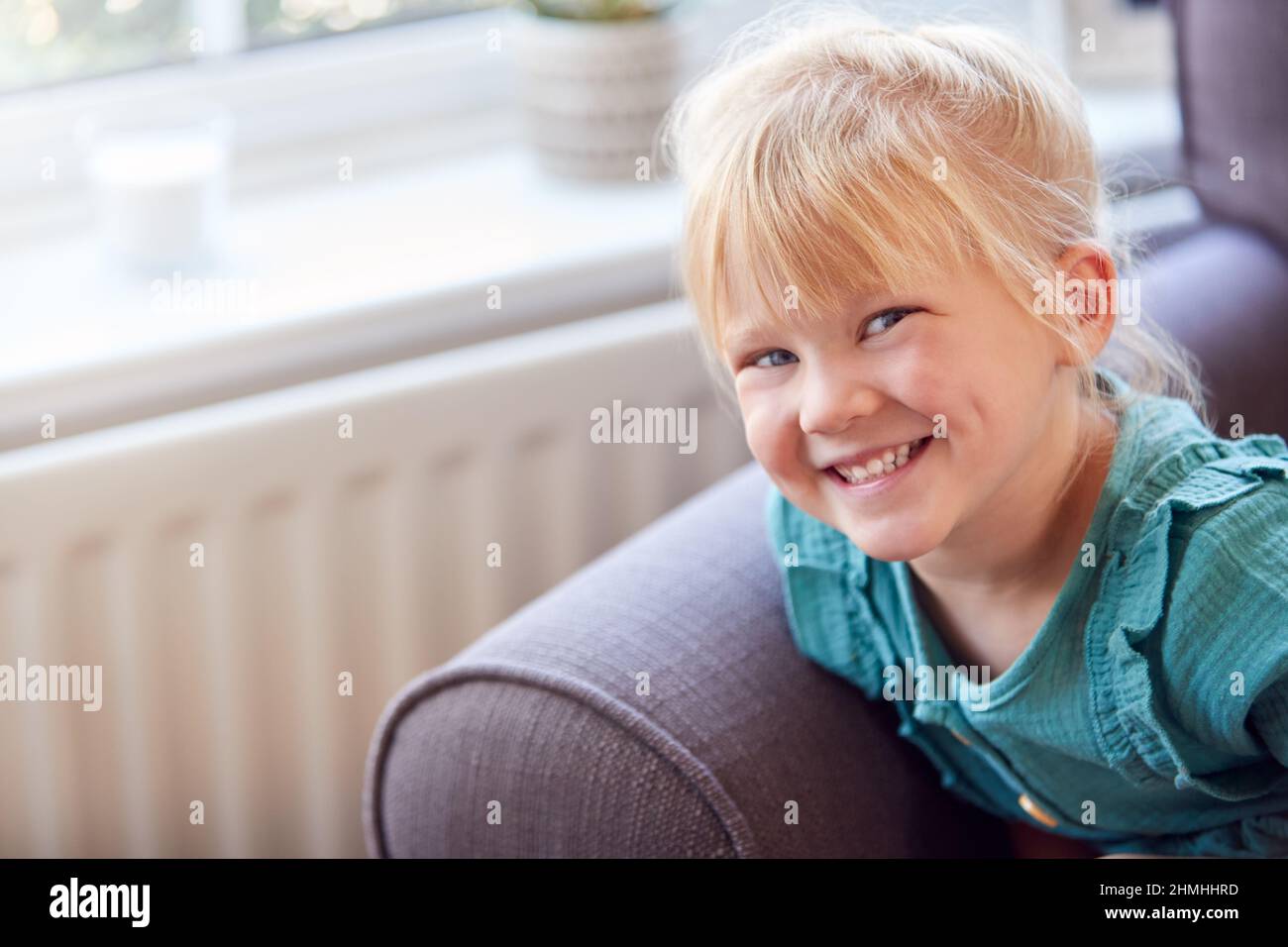Portrait Of Smiling Young Girl Sitting On Sofa In Lounge At Home ...