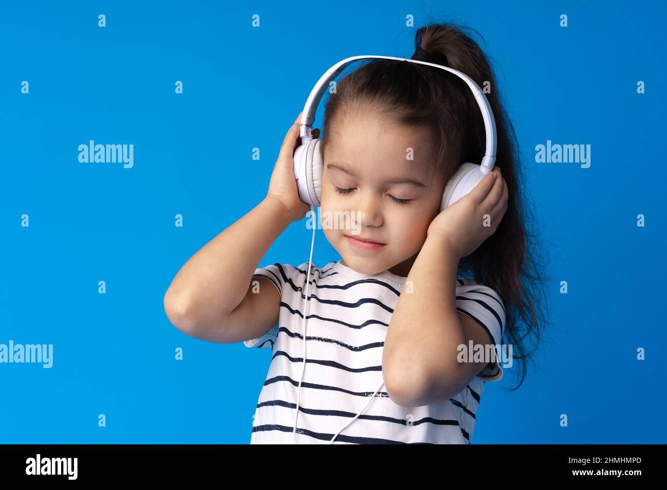 Little girl child wear headphones listen to music over blue background