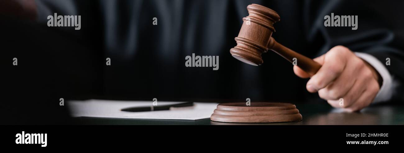 partial view of blurred judge holding gavel during sentencing, banner Stock Photo