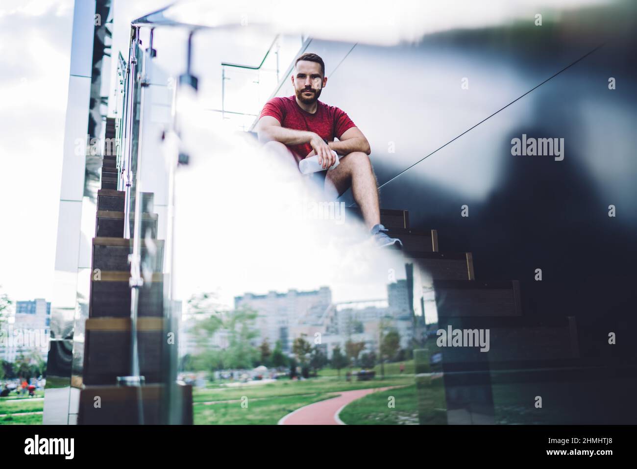 Young sportsman sitting on stairs with glass fence Stock Photo
