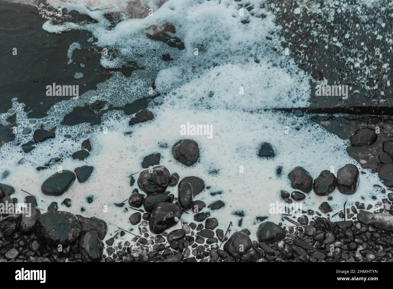 White foam water near the stone coast of lake foamy. Stock Photo