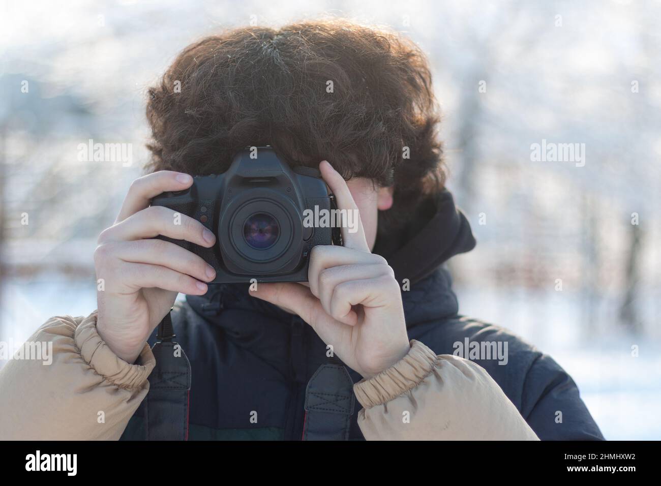A teenage boy with curly long hair takes a picture with a digital SLR ...