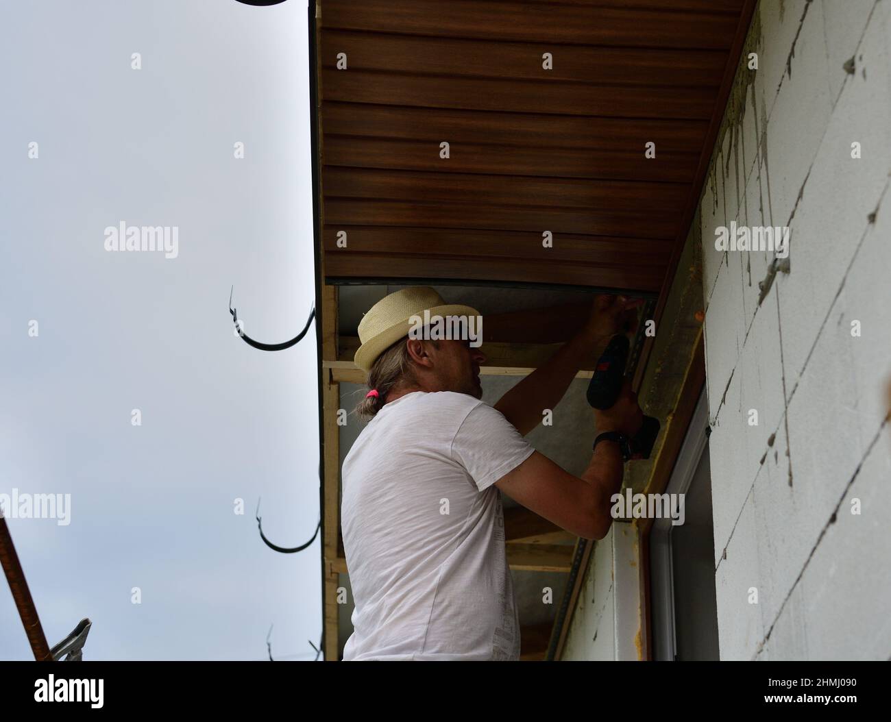 A carpenter screws on the roof soffit during the renovation of the
