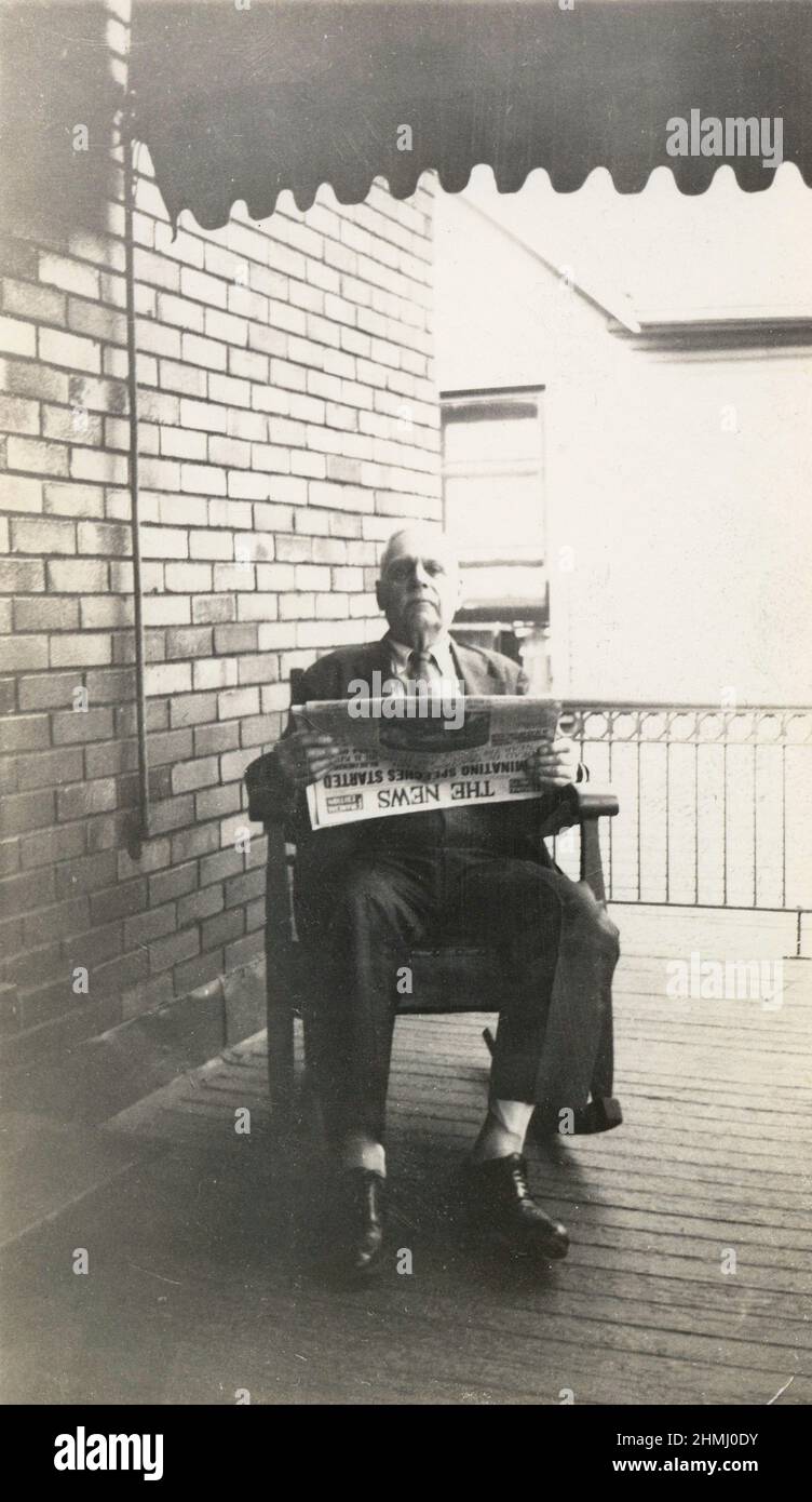 Antique circa 1910 photograph of an elderly man reading a newspaper in a rocking chair on his front porch. 'The News' was a newspaper in Dayton, Ohio. SOURCE: ORIGINAL PHOTOGRAPH Stock Photo