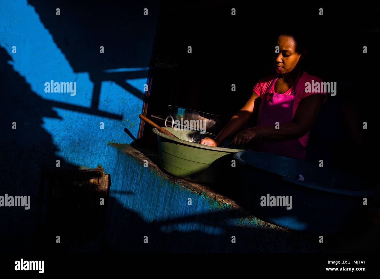 A young Afro-Colombian woman washes the dishes at the end of a twelve-hour shift in a street restaurant in the market of Bazurto, Cartagena, Colombia, Stock Photo