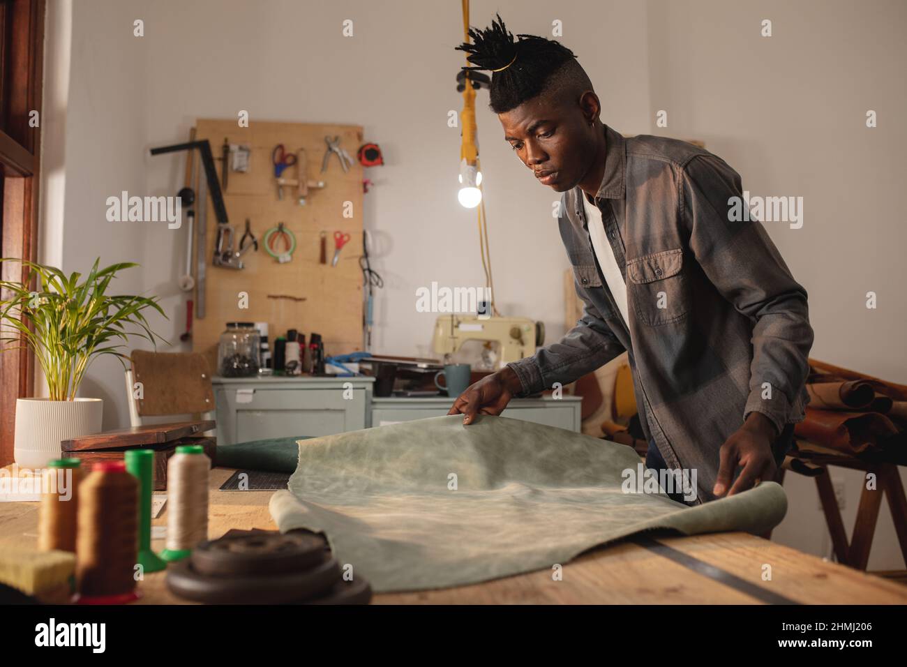 African american young craftsman keeping leather on workbench while working in workshop Stock Photo