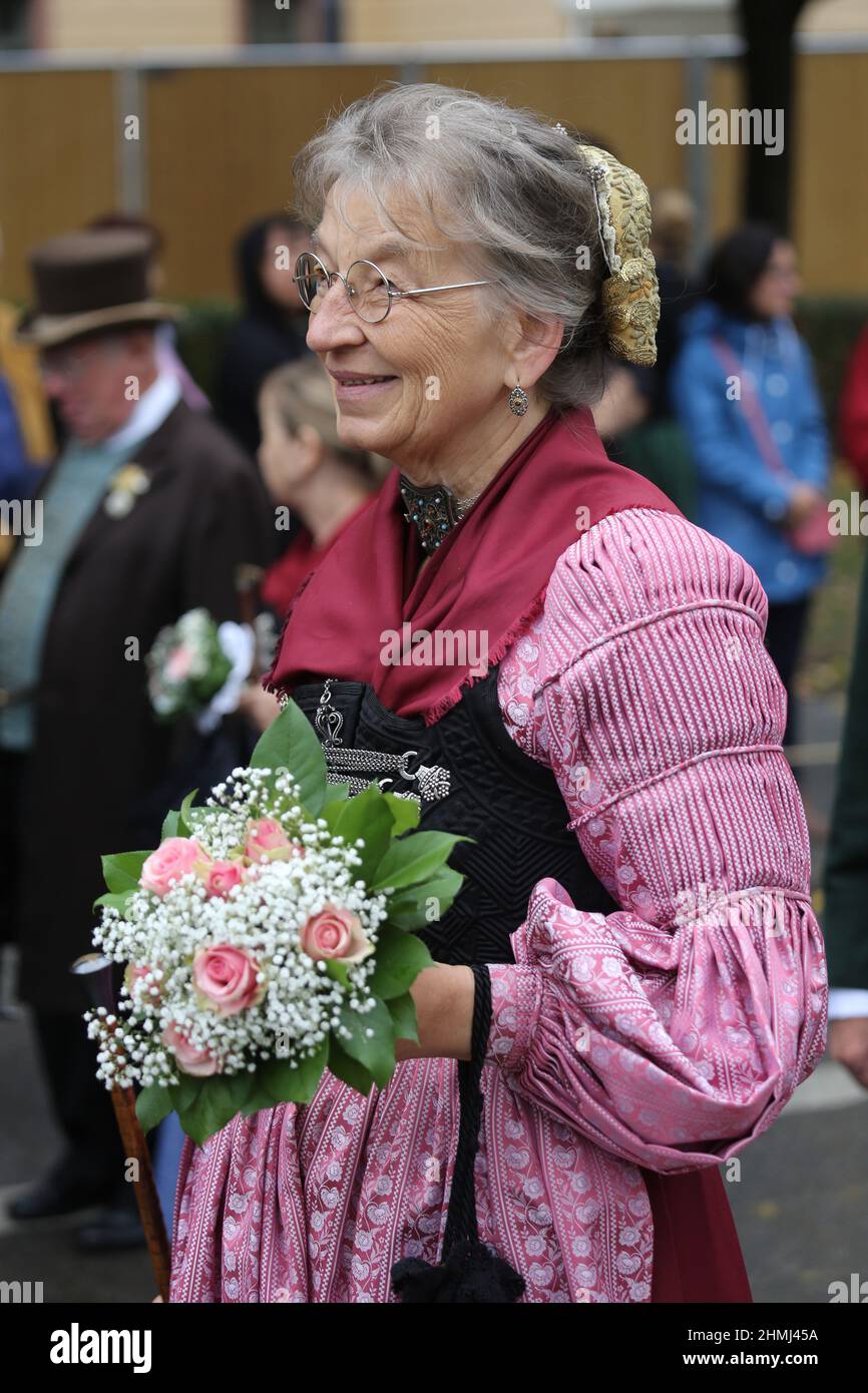 A woman wearing a traditional dirndl and carrying a bunch of flowers participates in the Oktoberfest parade in Munich Stock Photo