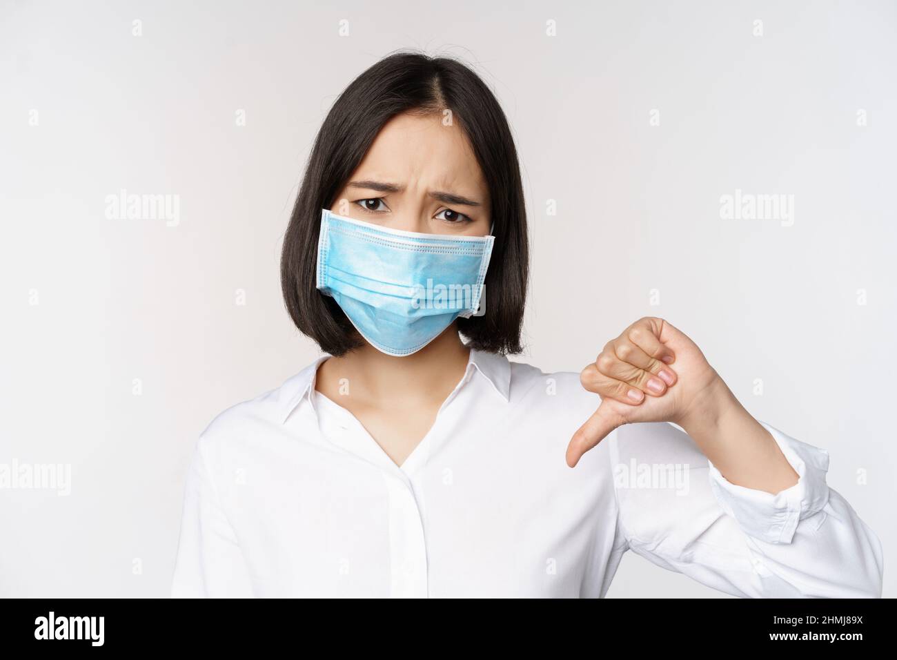 Portrait of asian woman in medical face mask showing thumbs down with ...