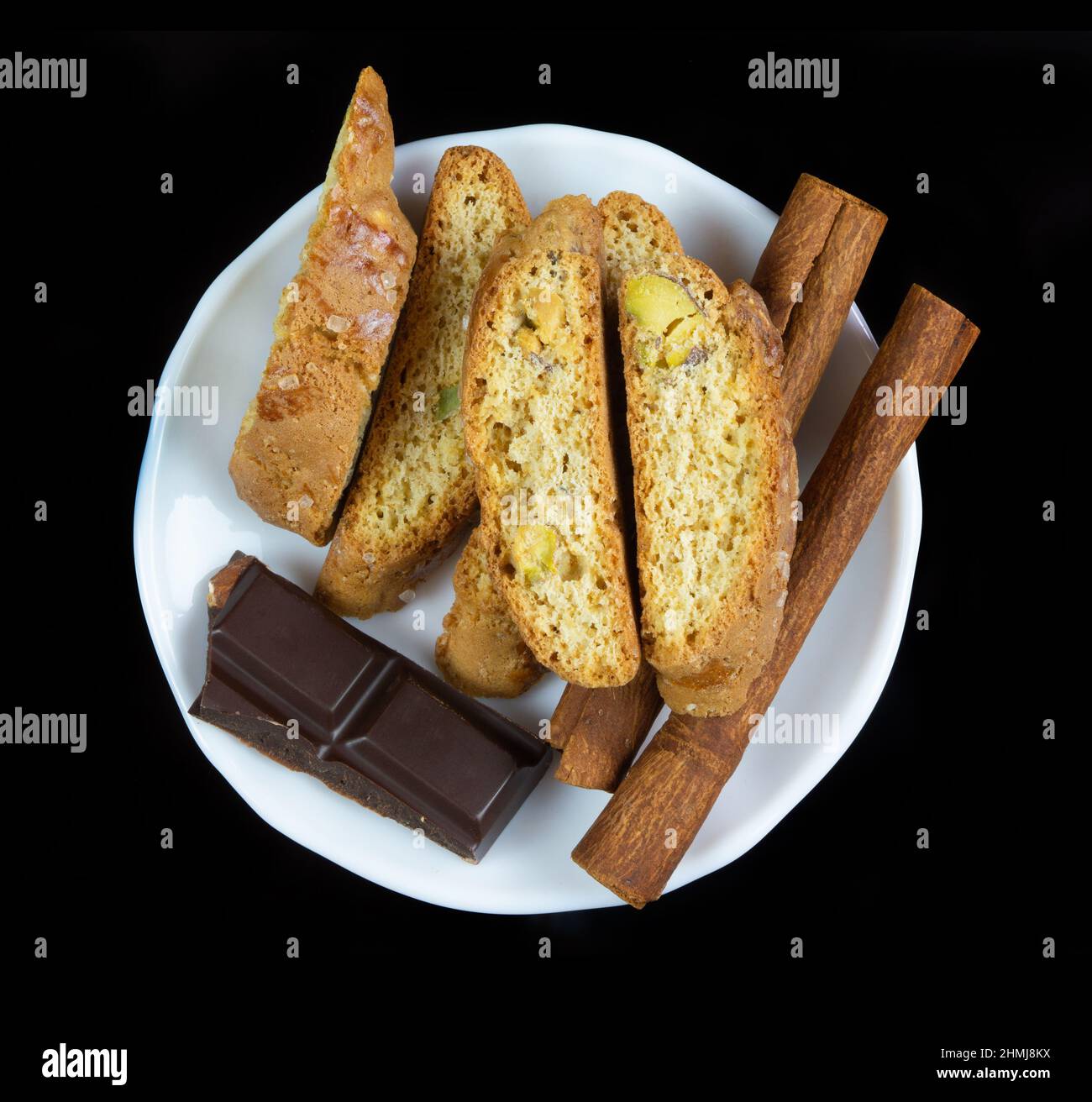 Cinnanon sticks, chocolate and bisquits in a white plate isolated over black background Stock Photo