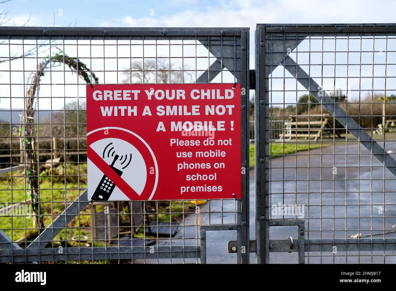 A school notice at a school gate asking parents not to use their mobile phones whilst collecting or dropping off children at school. Stock Photo