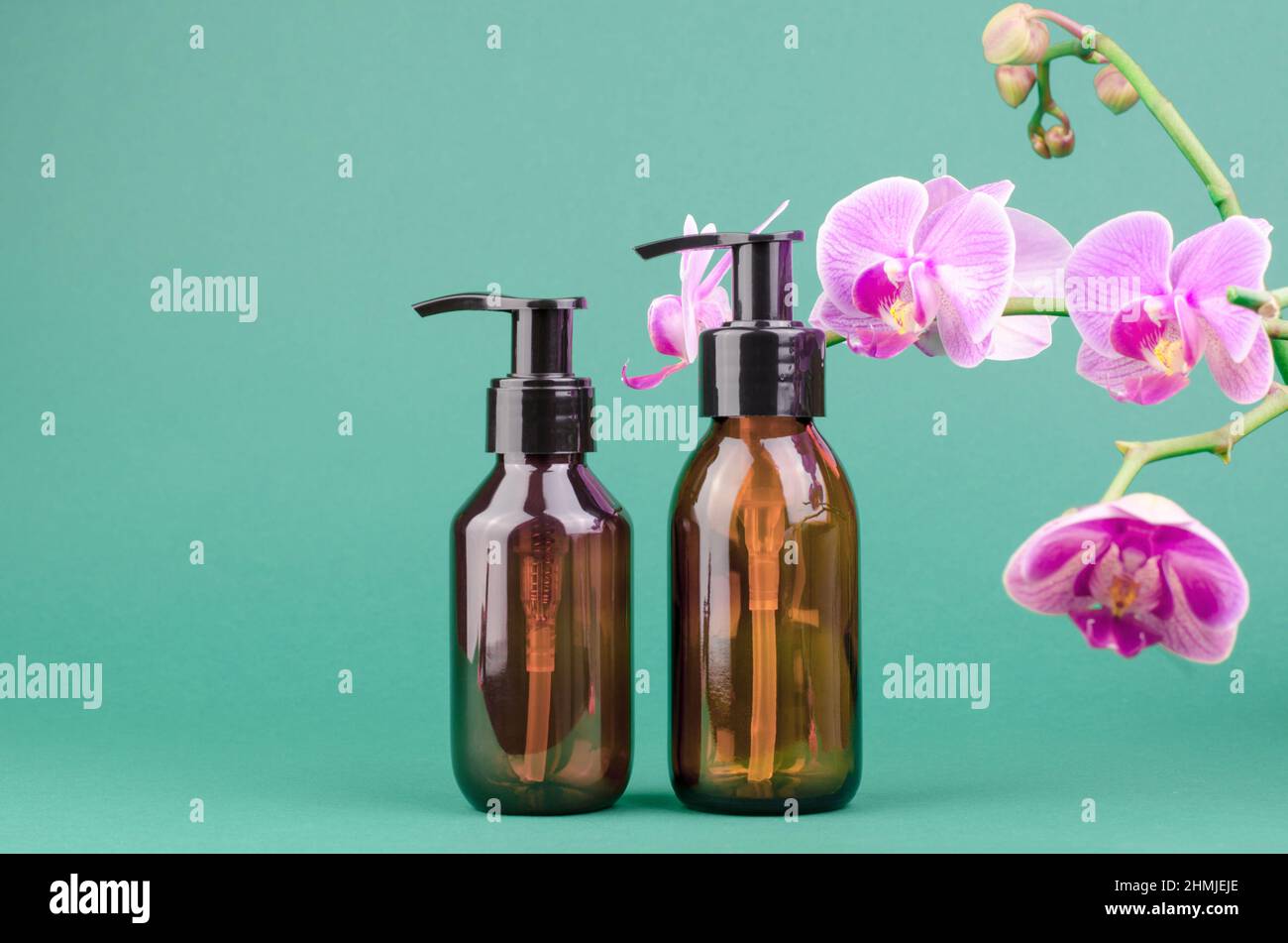 Cosmetic bottles with dispensers on a green background with orchid ...
