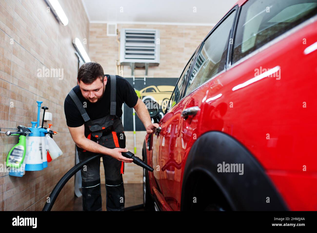 Man worker drying red car in detailing garage after washing Stock Photo