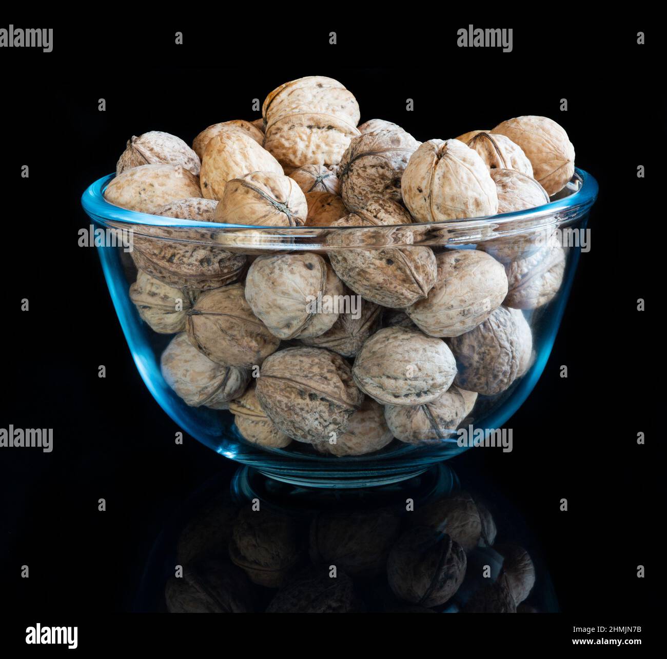 Whole solid walnuts in a glass bowl on black reflective background Stock Photo
