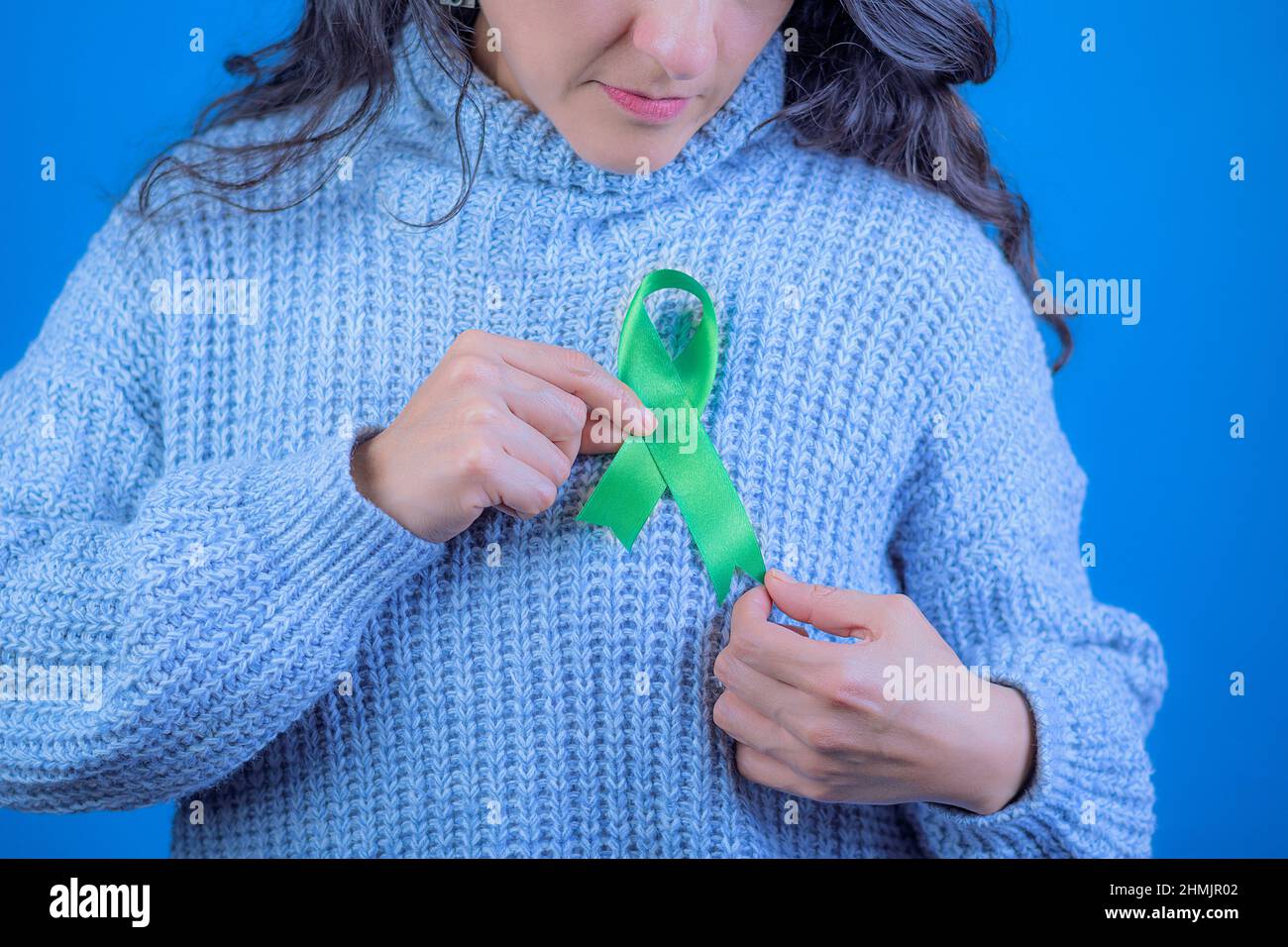 Green ribbon to support liver and adrenal cancer awareness, Human hands holding green ribbon. World Cancer Day. Space for text Stock Photo