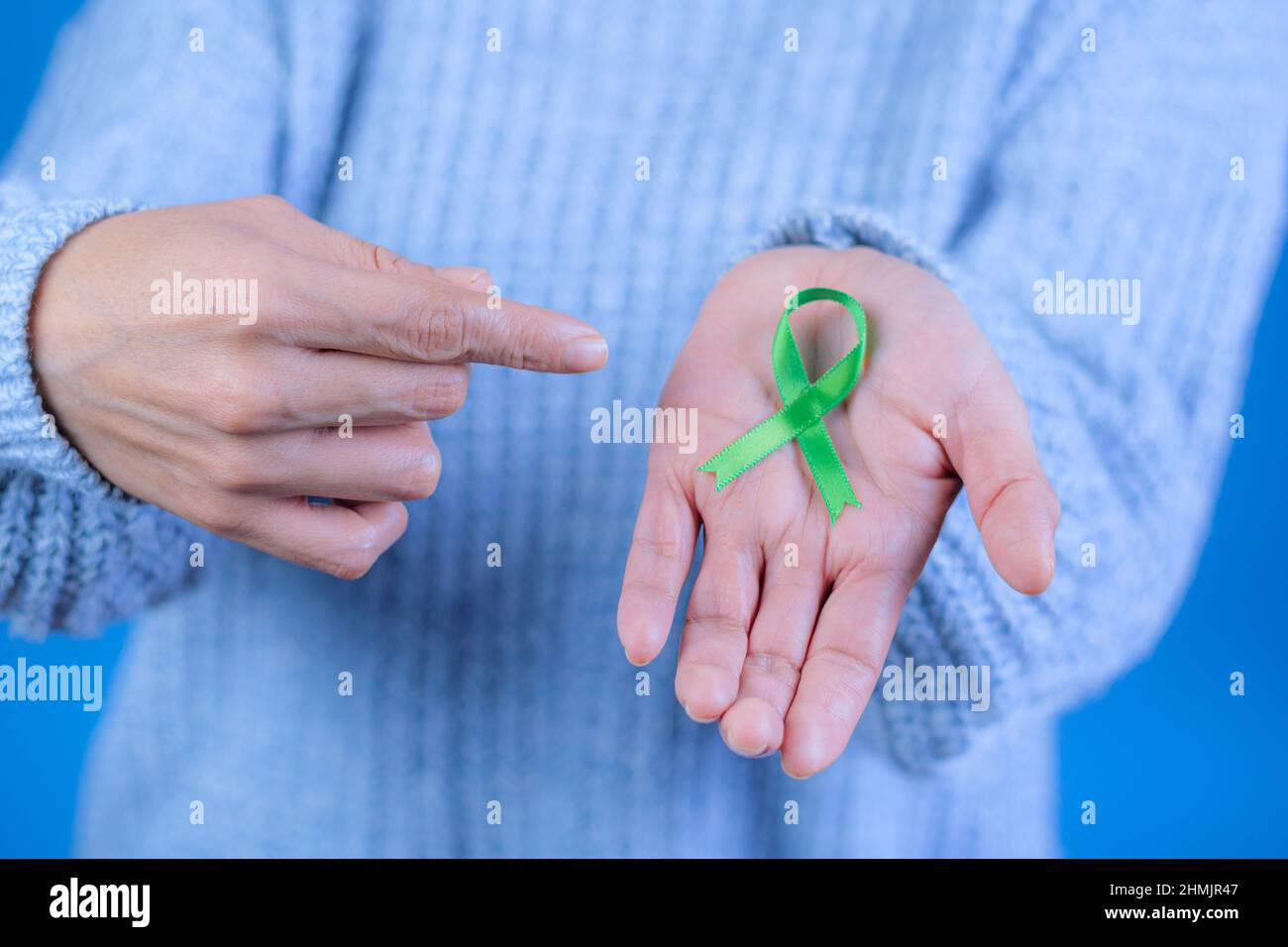 Green ribbon to support liver and adrenal cancer awareness, Human hands holding green ribbon. World Cancer Day. Space for text Stock Photo