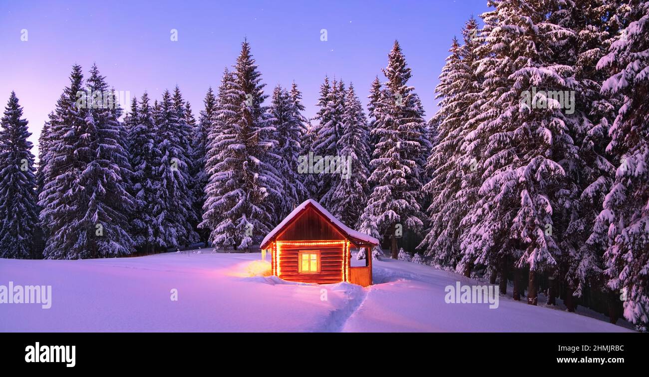 Panorama with wooden hut on the lawn covered with snow. Marry Christmas and New Year. The lamps light up the house at the evening time. Winter landsca Stock Photo