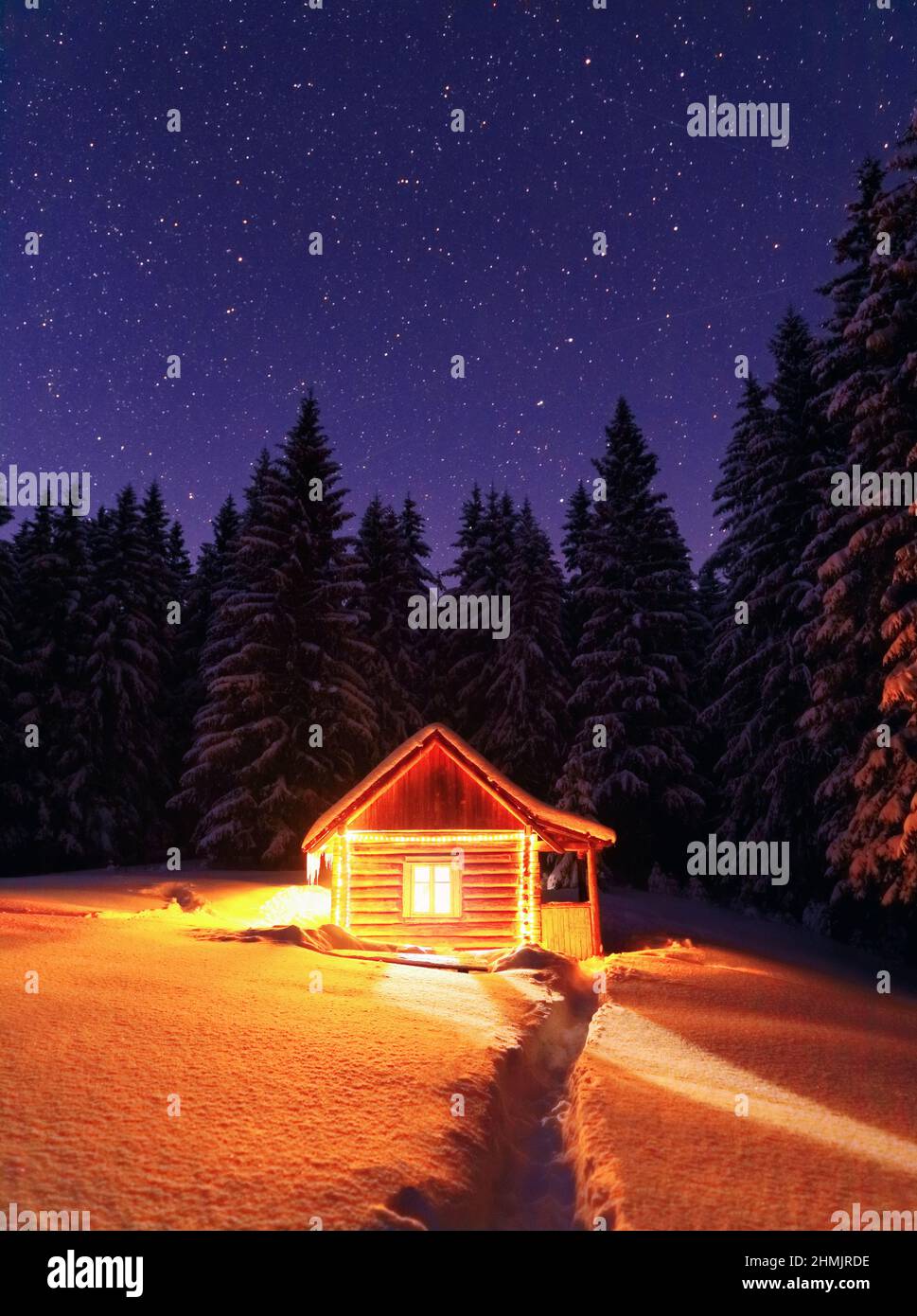 Wooden hut on the lawn covered with snow. Marry Christmas and New Year. The lamps light up the house at the evening time. Winter landscape. Mystical n Stock Photo