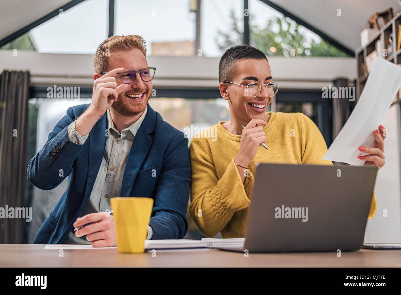 Young successful diverse couple sitting in living room or kitchen discussing new home project using laptop working and planing calculating home financ Stock Photo