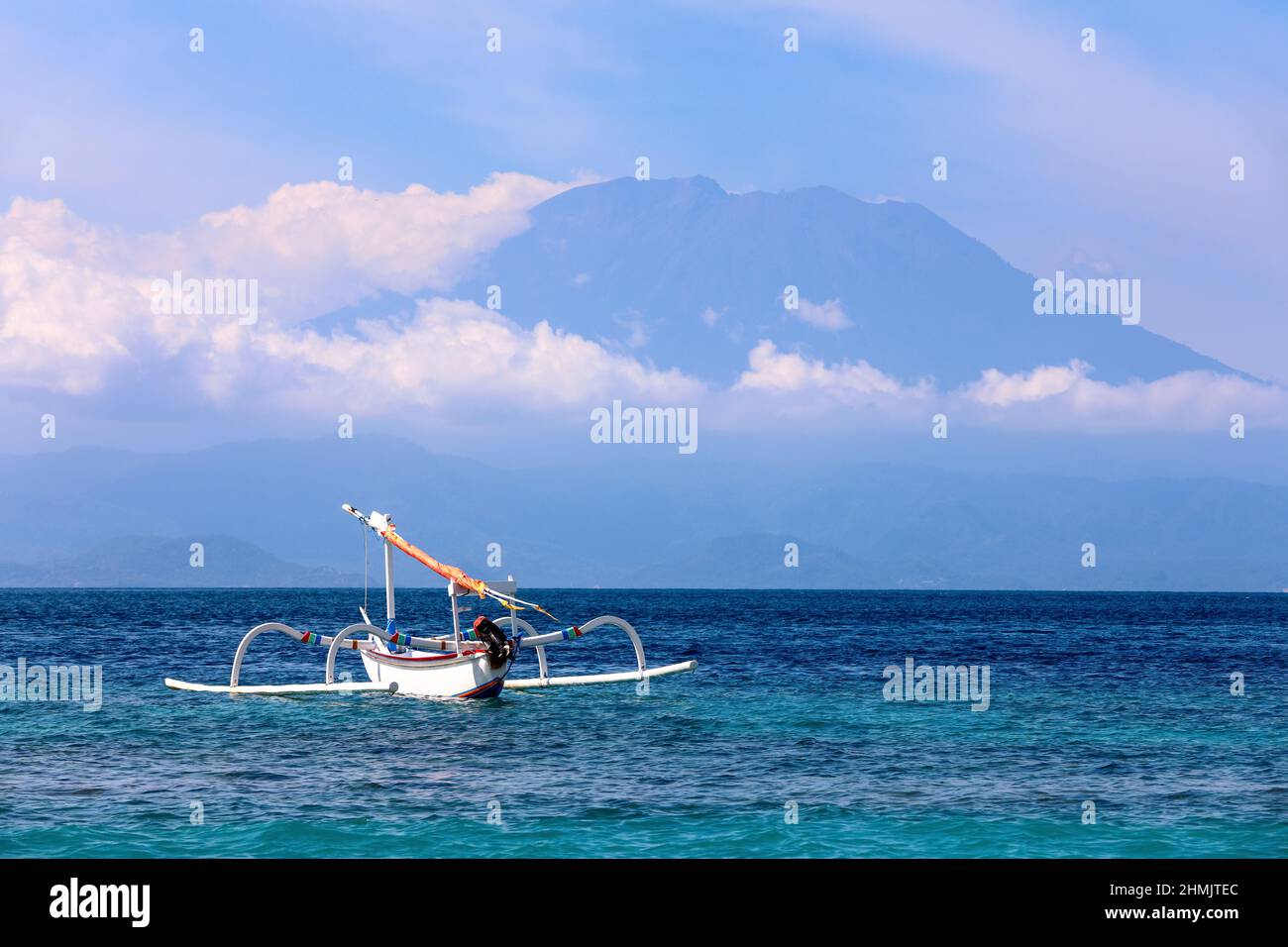 Mount Agung active volcano covered by clouds in Nusa Penida, Bali island, Indonesia. Traditional fishing boats called jukung on the white sand beach. Stock Photo