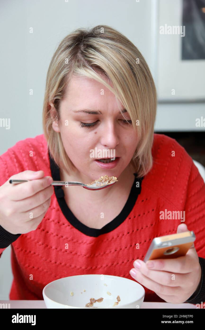 A young female eating breakfast cereal and looking at her phone. Stock Photo