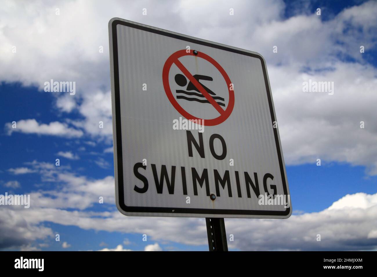 The No Swimming sign with the icon and a blue and white sky behind during a sunny day Stock Photo