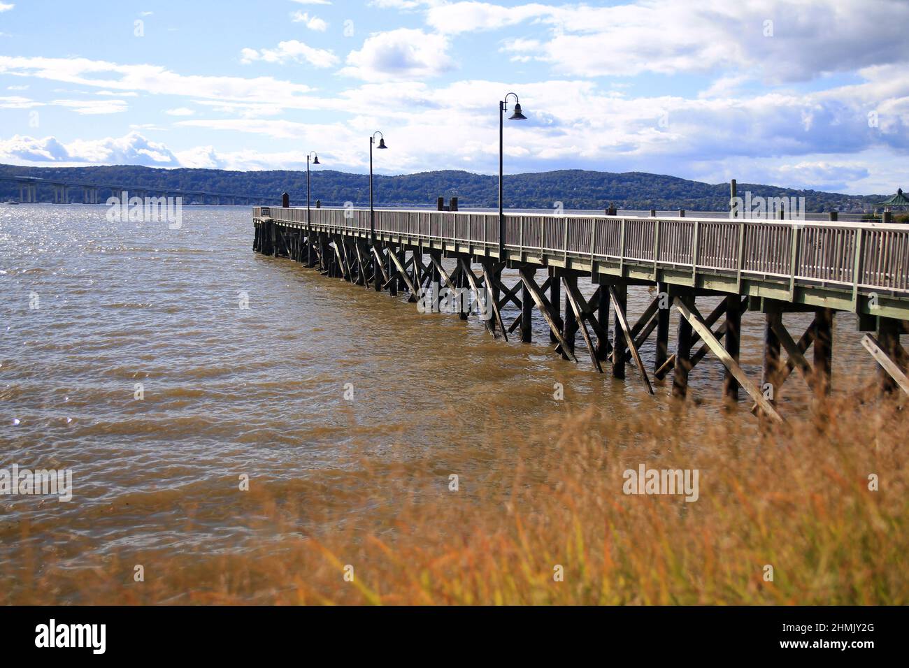 The wooden pier emerging from the fall bushes on the river during a sunny and clouded day Stock Photo