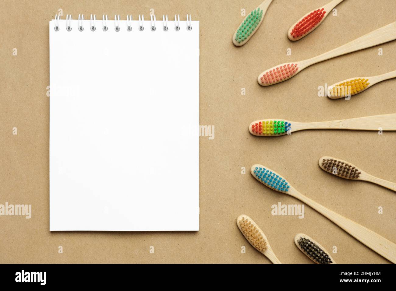 Multiple multicolor bamboo toothbrushes are lying on craft eco paper with notepad. Copy space, top view. Stock Photo