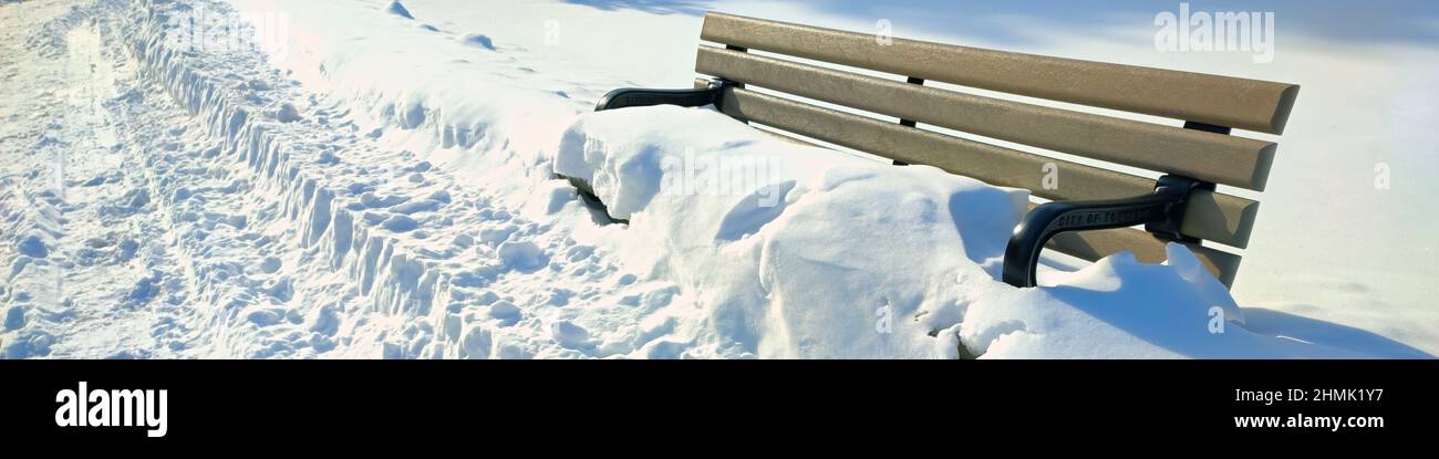 Panoramic web banner of a park bench covered in deep snow in the park. Stock Photo