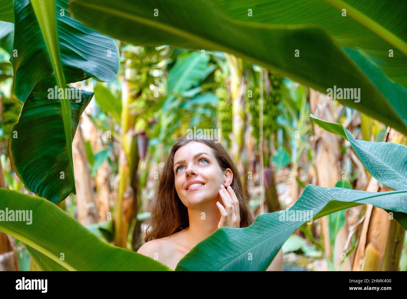 Beautiful young caucasian brunette long hair woman portrait near banana palm leaves tropical plants in jungle. Skin care and natural organic beauty Stock Photo