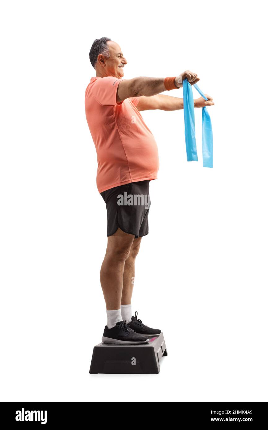 Full length profile shot of a mature man in sportswear exercising with a stretch strap on a step aerobic platform isolated on white background Stock Photo