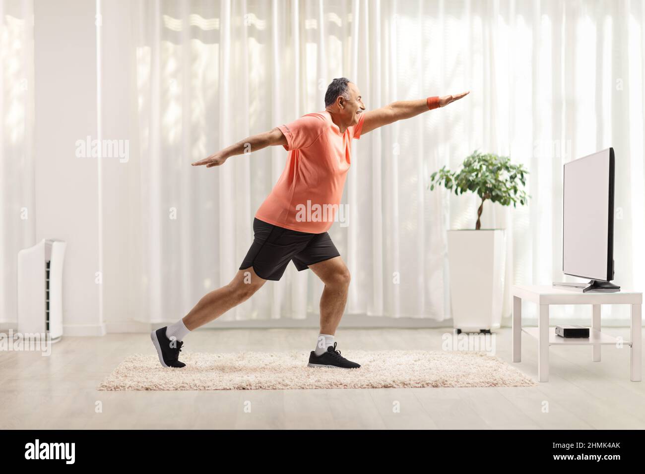 Full length shot of a mature man in sportswear exercising and stretching in front of tv at home Stock Photo