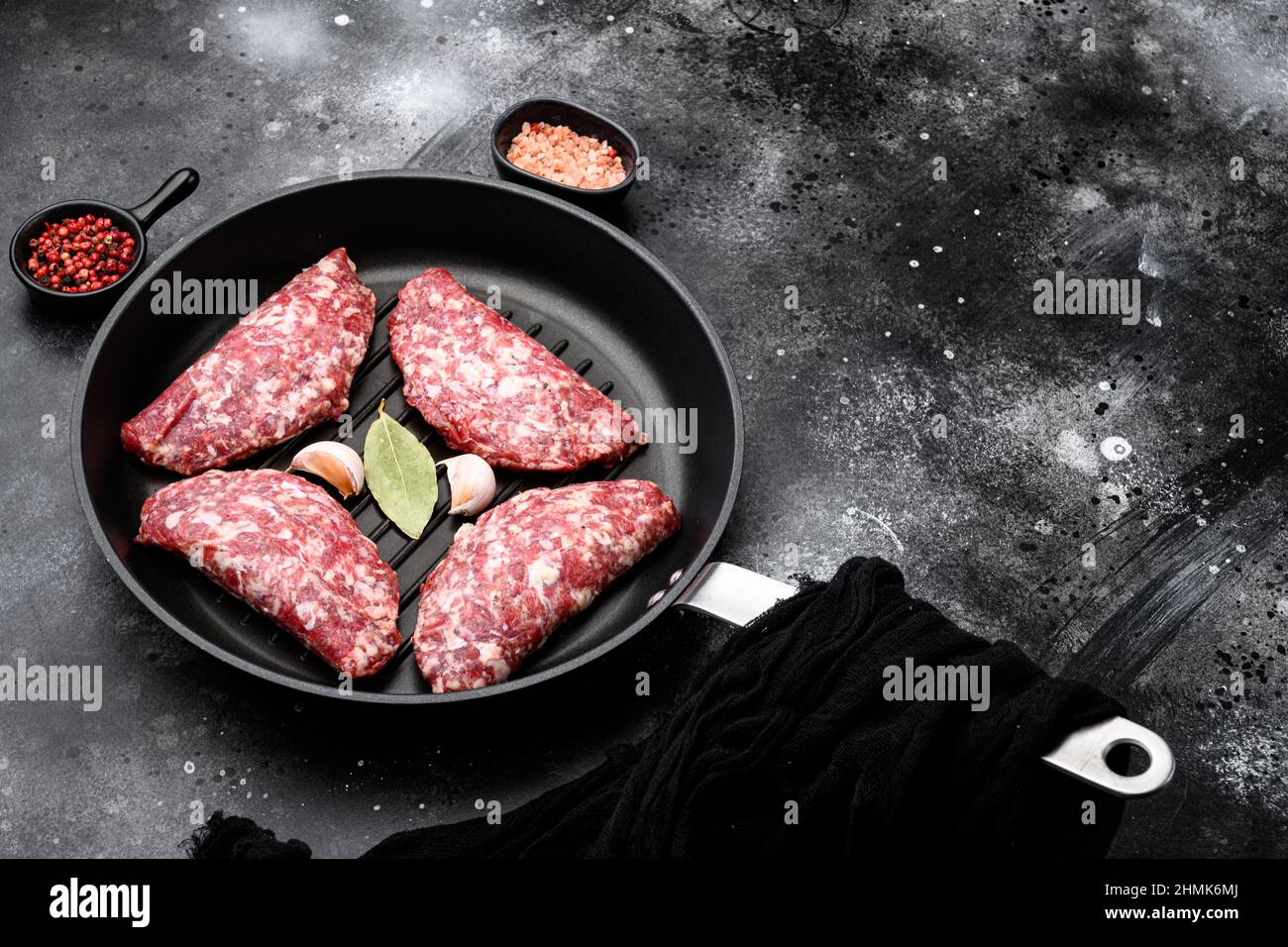 Raw meat, cutlet set, in cast iron frying pan, on black dark stone table background, with copy